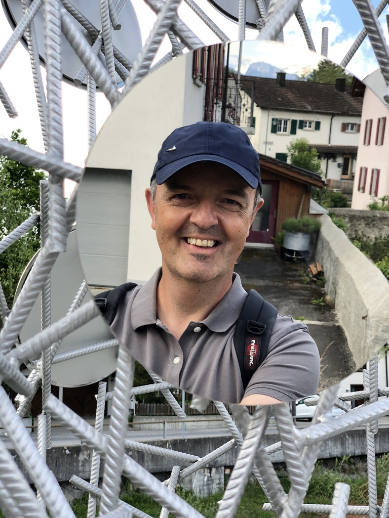 Bruno Fluder in einem runden Spiegelbild mit Häusern im Hintergrund.