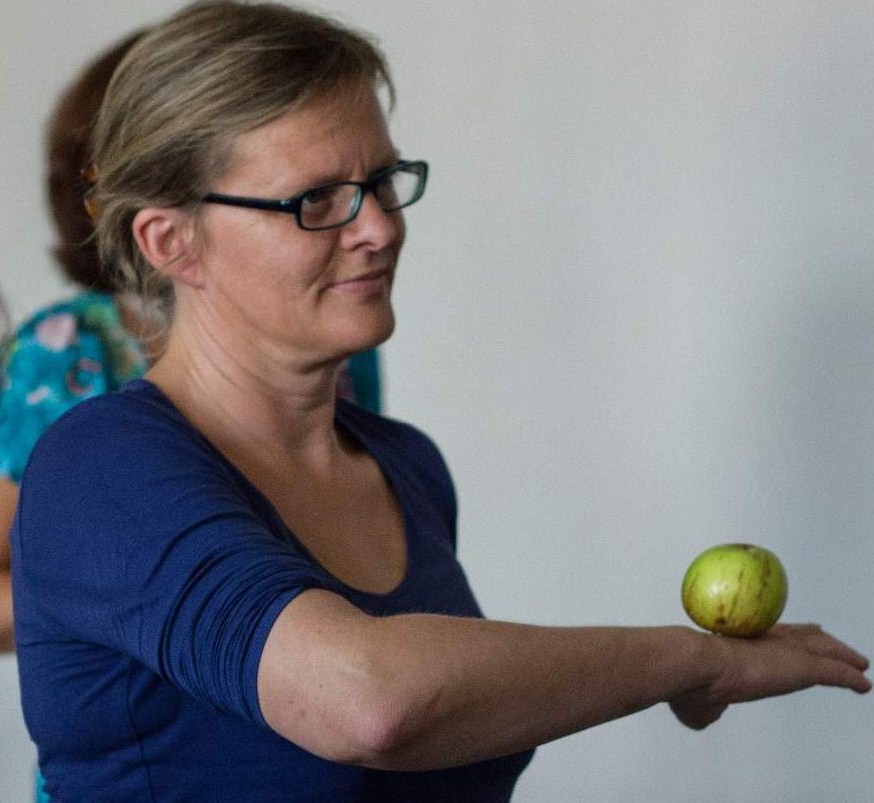 Harder Maria balanciert einen Apfel auf dem Handrücken. Im Hintergrund sind unscharf weitere Workshop-Teilnehmende zu sehen.