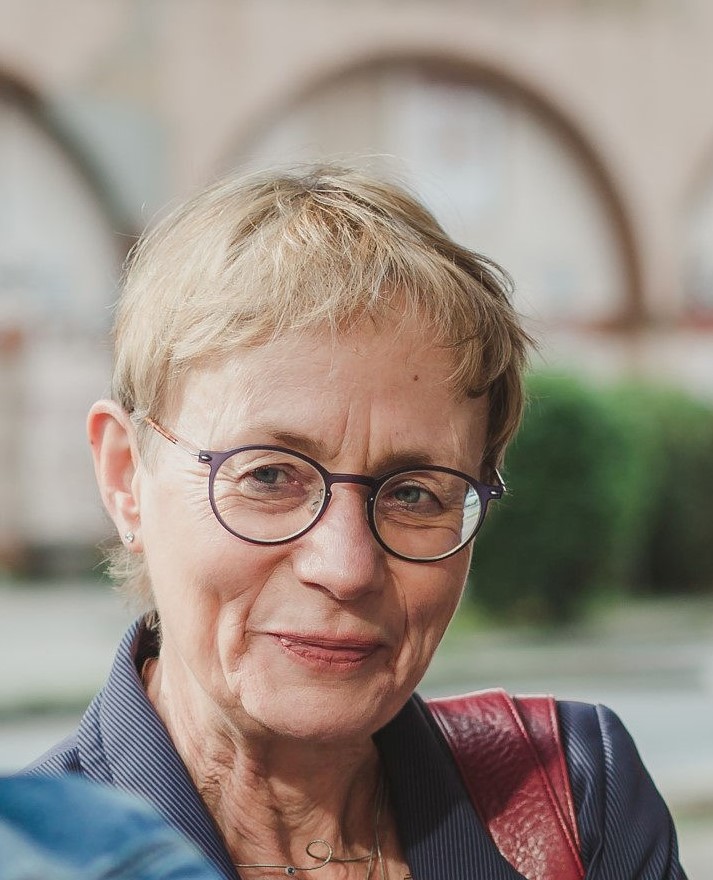 Regine Gittinger mit umgehängter Tasche, lächelnd, im Hintergrund unscharf Torbögen zu erkennen